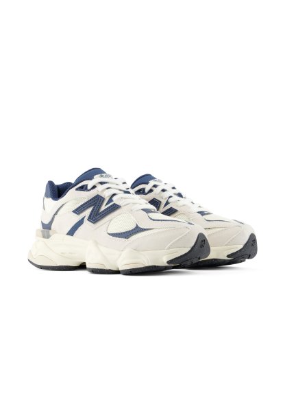 Par de zapatillas deportivas blancas y azul marino con suelas gruesas y detalles de logotipos en los laterales y la lengüeta, mostradas sobre un fondo blanco.
