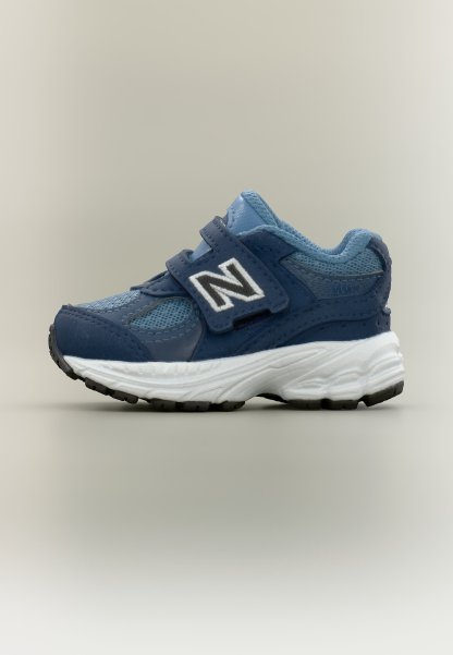 Zapatilla deportiva para niño pequeño en azul y azul marino con suela blanca, detalles de malla y cuero, y una correa de velcro con el logo blanco de la letra N.