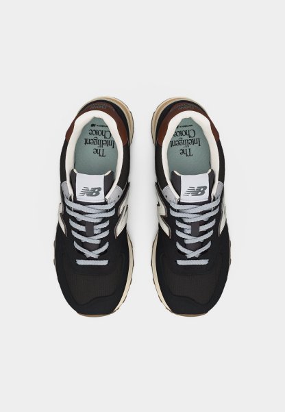 Par de zapatillas New Balance en blanco y negro con cordones grises, suelas beige y plantilla azul verdosa con la etiqueta "La Elección Inteligente".