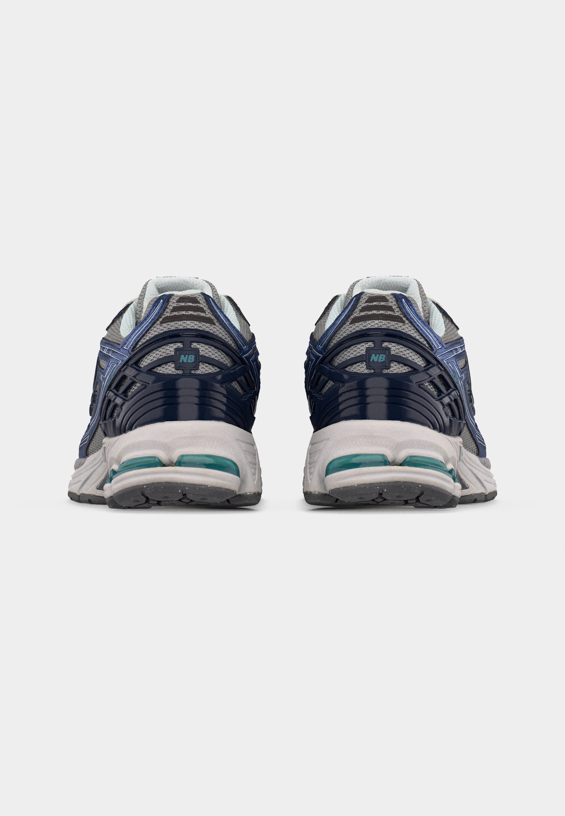 Par de zapatillas de correr grises y azul marino con suelas blancas vistas desde atrás sobre un fondo claro y sencillo.