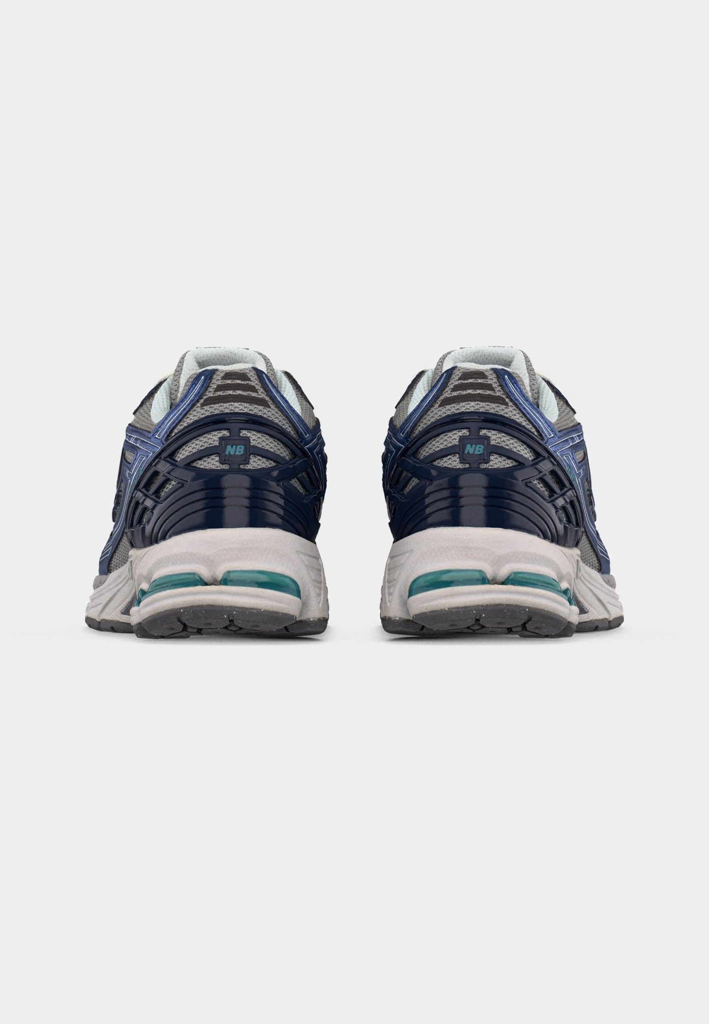 Par de zapatillas de correr grises y azul marino con suelas blancas vistas desde atrás sobre un fondo claro y sencillo.