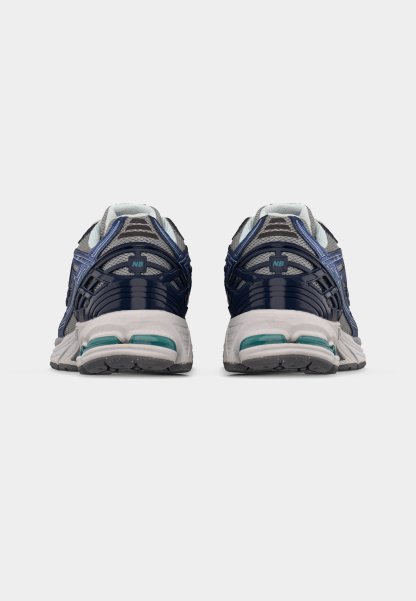 Par de zapatillas de correr grises y azul marino con suelas blancas vistas desde atrás sobre un fondo claro y sencillo.