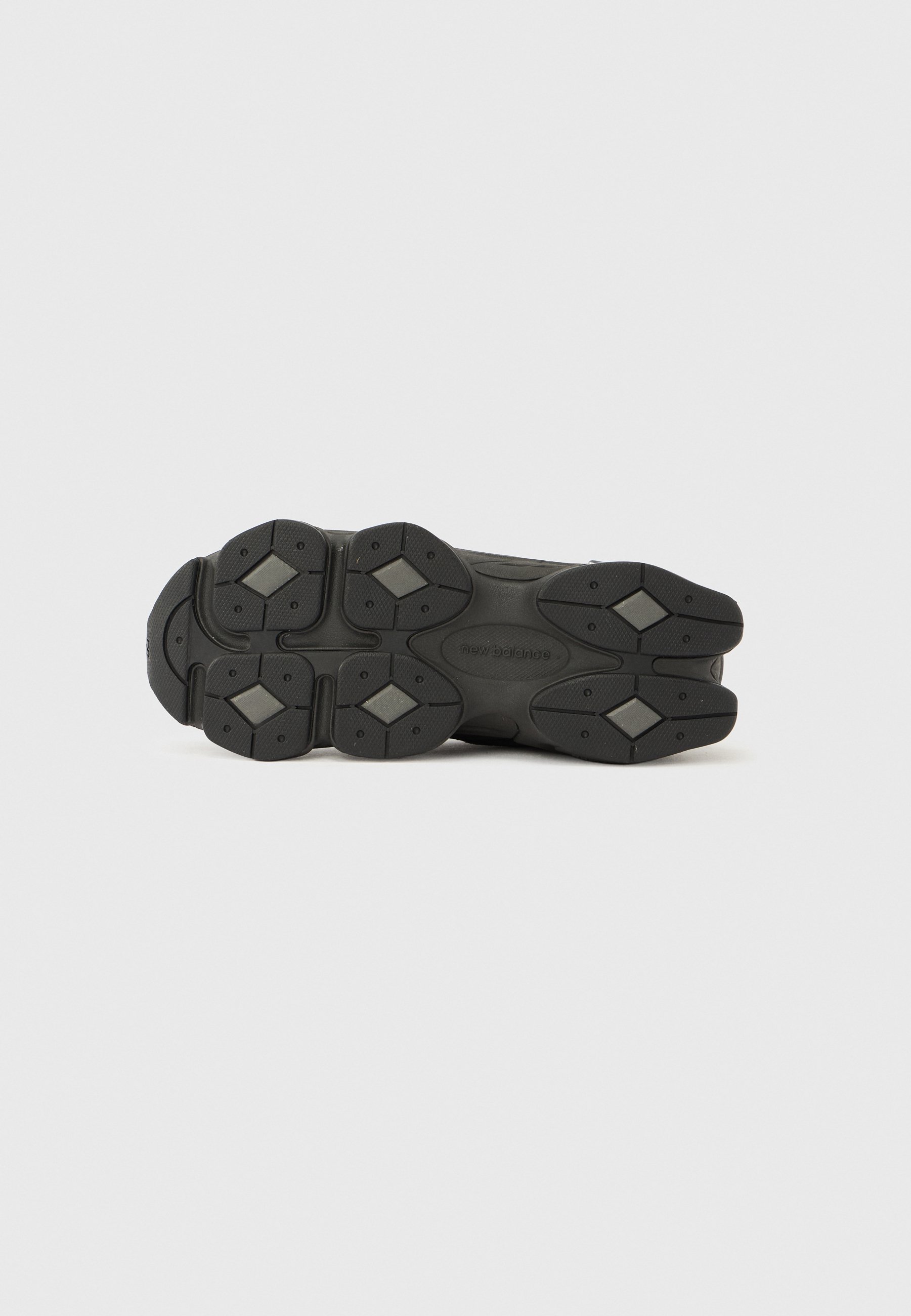 Suela de zapato deportivo negra con superficie texturizada, múltiples formas contorneadas y patrones de agarre de goma hexagonales. Etiquetada "new balance."