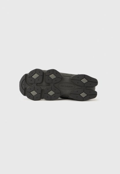 Suela de zapato deportivo negra con superficie texturizada, múltiples formas contorneadas y patrones de agarre de goma hexagonales. Etiquetada "new balance."
