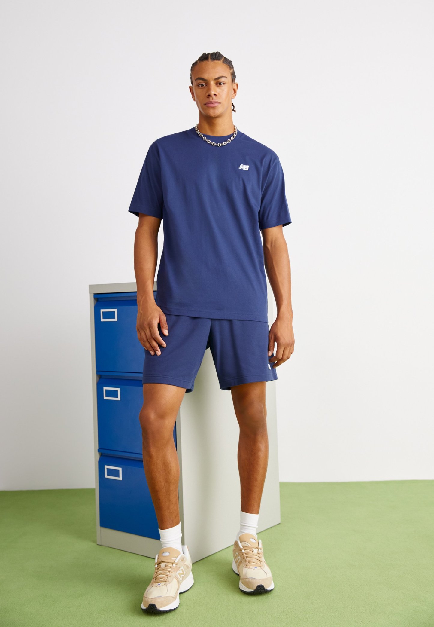 Conjunto de camiseta de color azul marino y pantalones cortos hecho de una tela suave, que presenta un pequeño logo en el pecho. El modelo está de pie junto a un archivador.