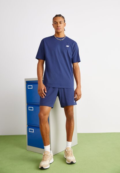 Conjunto de camiseta de color azul marino y pantalones cortos hecho de una tela suave, que presenta un pequeño logo en el pecho. El modelo está de pie junto a un archivador.