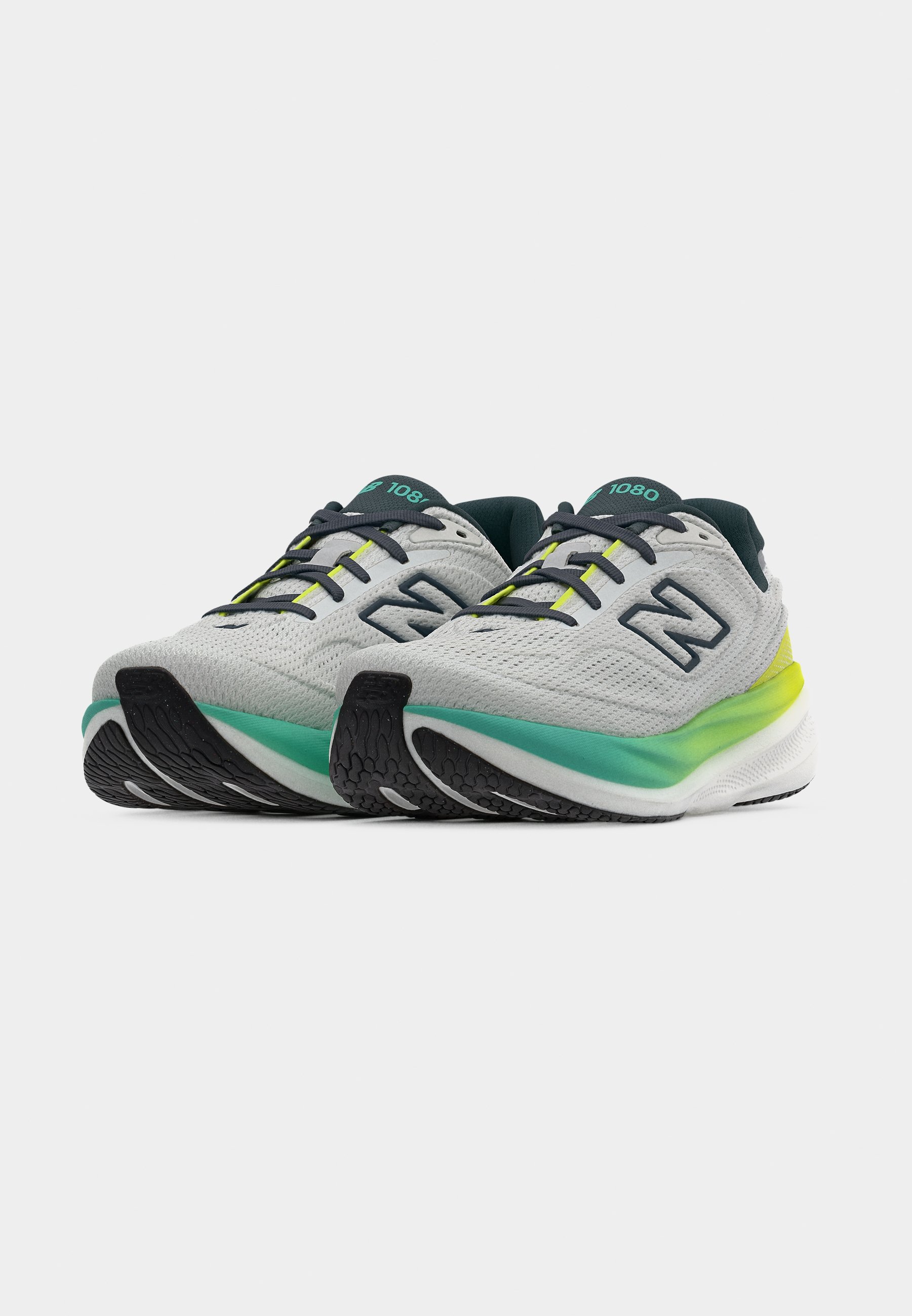 Par de zapatillas de correr blancas con cordones negros, medias suelas en degradado verde y amarillo, y suela exterior negra sobre fondo blanco.