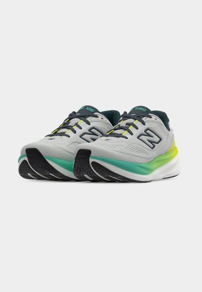 Par de zapatillas de correr blancas con cordones negros, medias suelas en degradado verde y amarillo, y suela exterior negra sobre fondo blanco.
