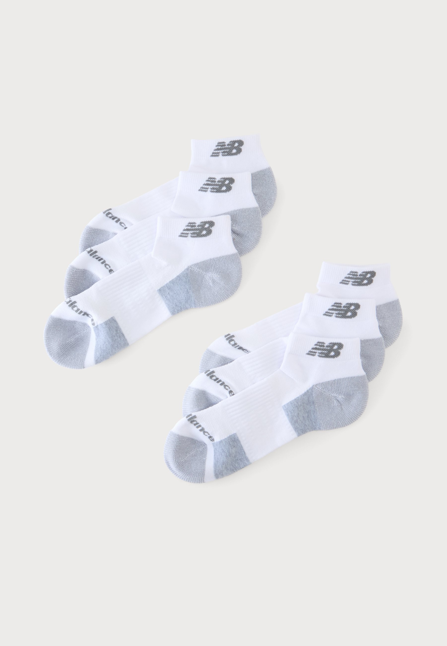 Dos juegos de tres calcetines blancos hasta el tobillo con talones y punteras grises, cada uno con un logo negro de New Balance en el tobillo.
