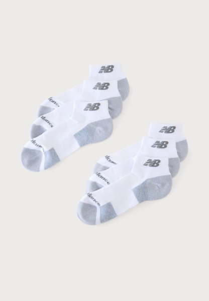 Dos juegos de tres calcetines blancos hasta el tobillo con talones y punteras grises, cada uno con un logo negro de New Balance en el tobillo.