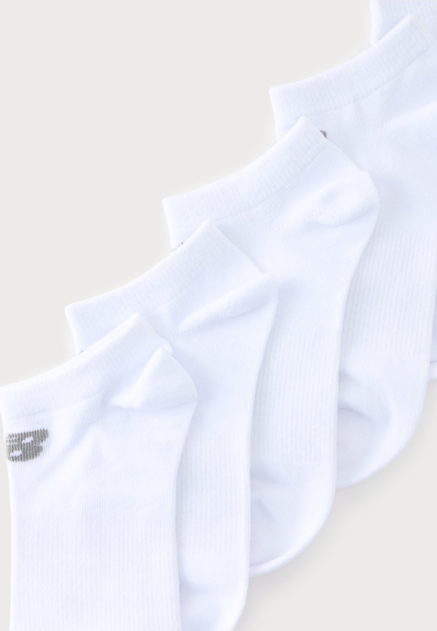 Cuatro pares de calcetines blancos tobilleros dispuestos en diagonal, con un pequeño logo gris visible en la puntera del par más delantero.
