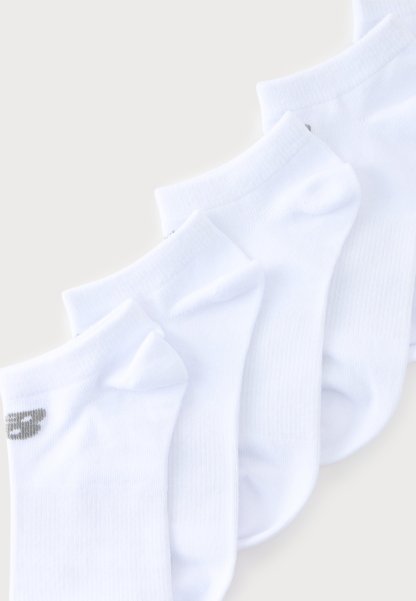 Cuatro pares de calcetines blancos tobilleros dispuestos en diagonal, con un pequeño logo gris visible en la puntera del par más delantero.