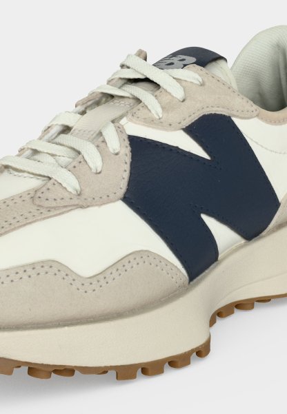 Zapatilla de correr con ante beige, cuero blanco, logo lateral azul marino, cordones blancos y suela de goma.