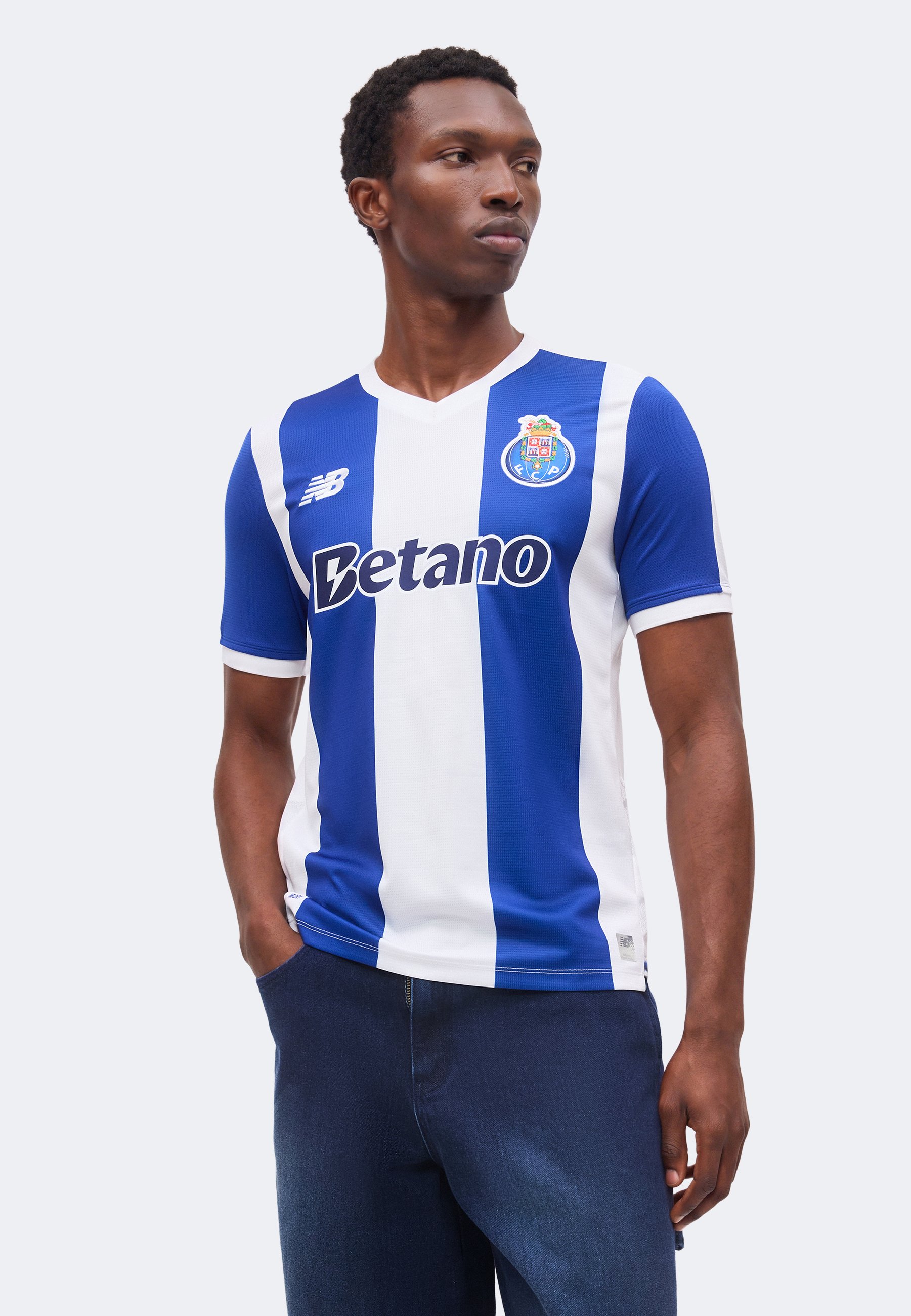 Hombre vistiendo la camiseta de fútbol del FC Porto con rayas verticales azules y blancas y logo del patrocinador, de pie con una mano en el bolsillo mirando de lado.