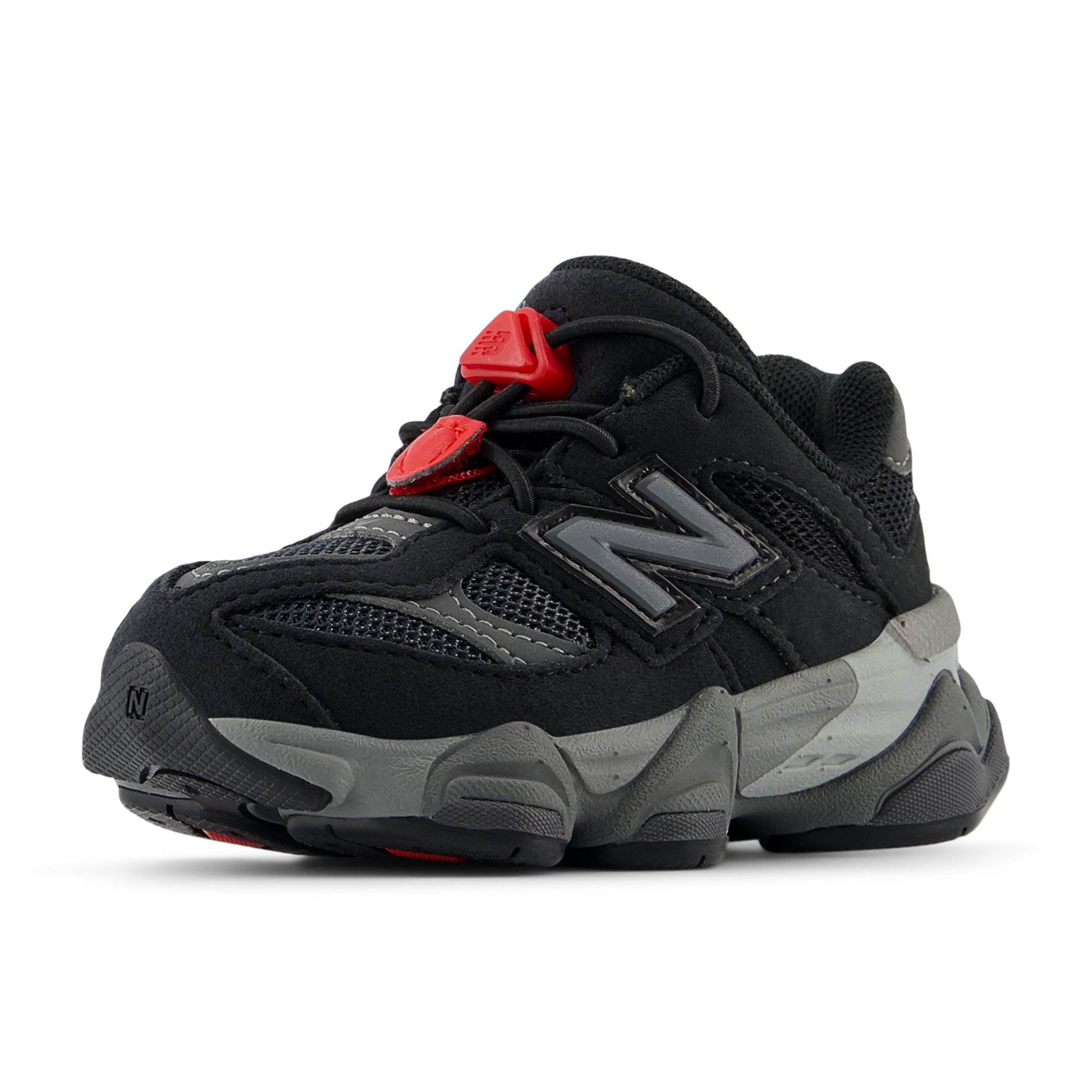 Zapatilla deportiva negra con materiales de malla y ante, con un prominente logo N gris, acentos rojos y una suela de goma texturizada.