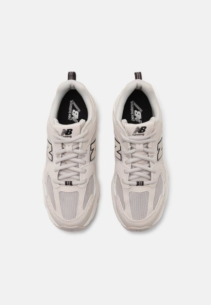 Zapatillas de running gris claro que presentan materiales de malla y sintéticos, con acentos negros y un distintivo logo "N" en los laterales.