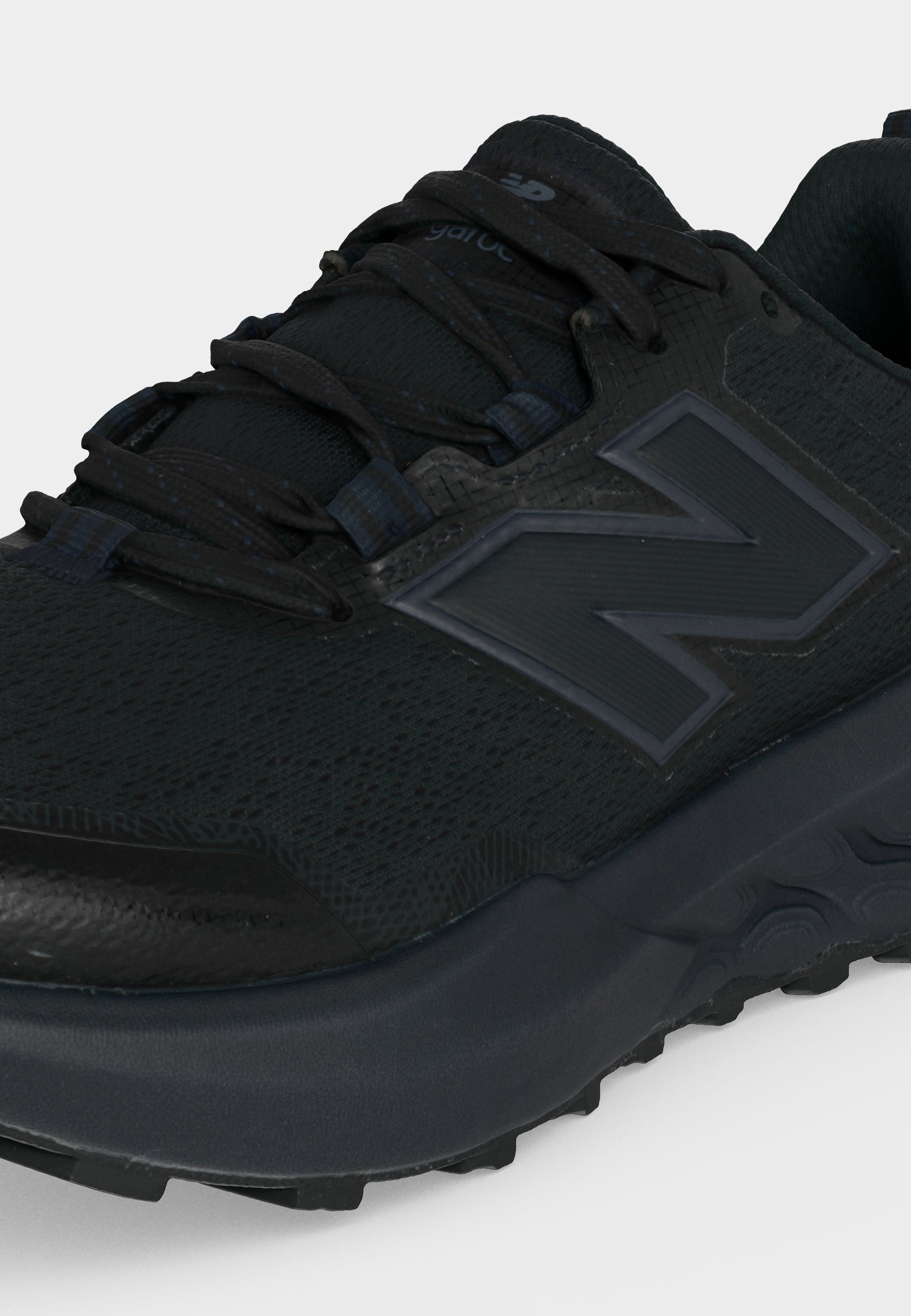 Primer plano de una zapatilla deportiva negra New Balance con tejido texturizado, suela gruesa y logo en el lateral, vista desde el ángulo frontal superior.