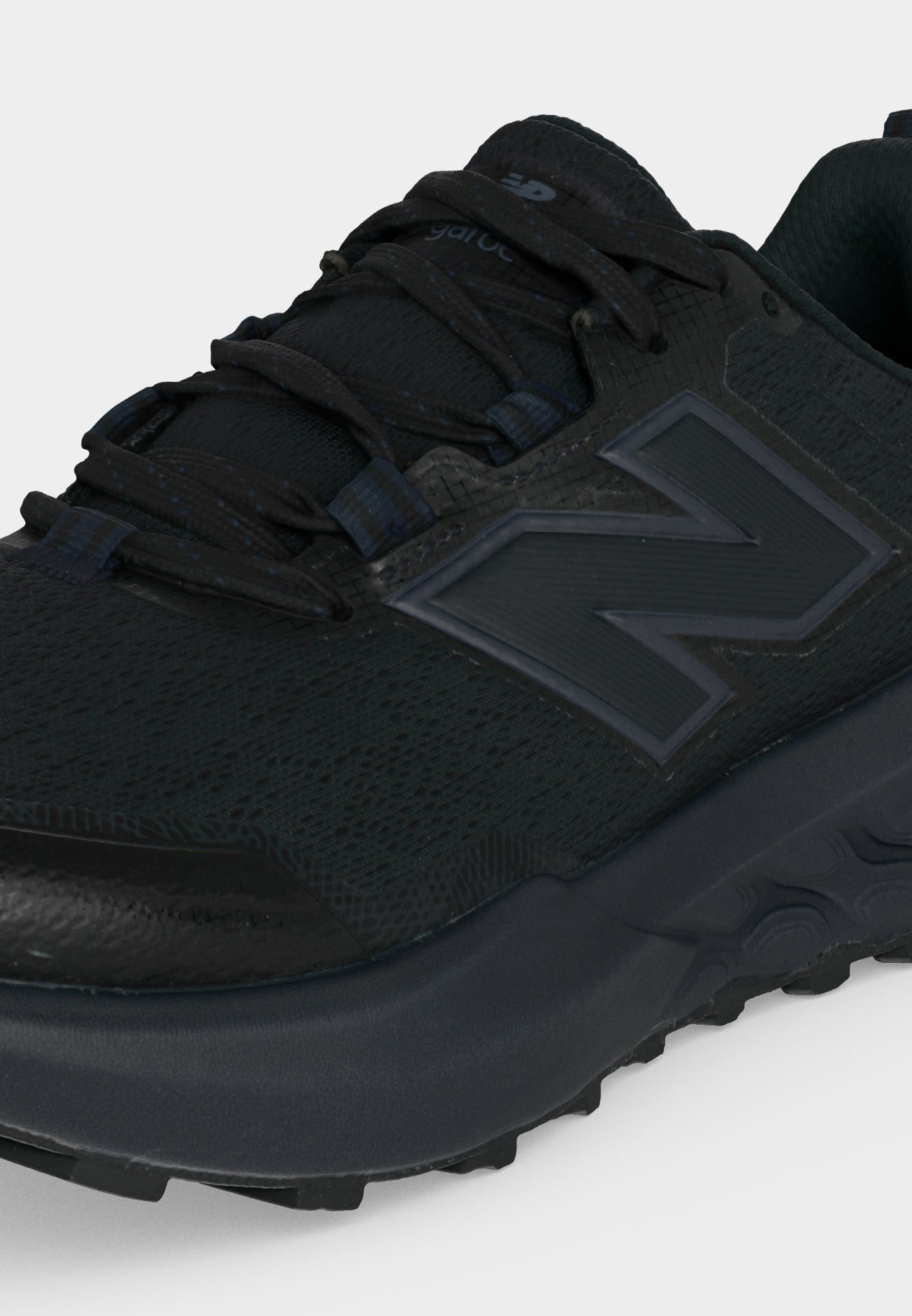 Primer plano de una zapatilla deportiva negra New Balance con tejido texturizado, suela gruesa y logo en el lateral, vista desde el ángulo frontal superior.