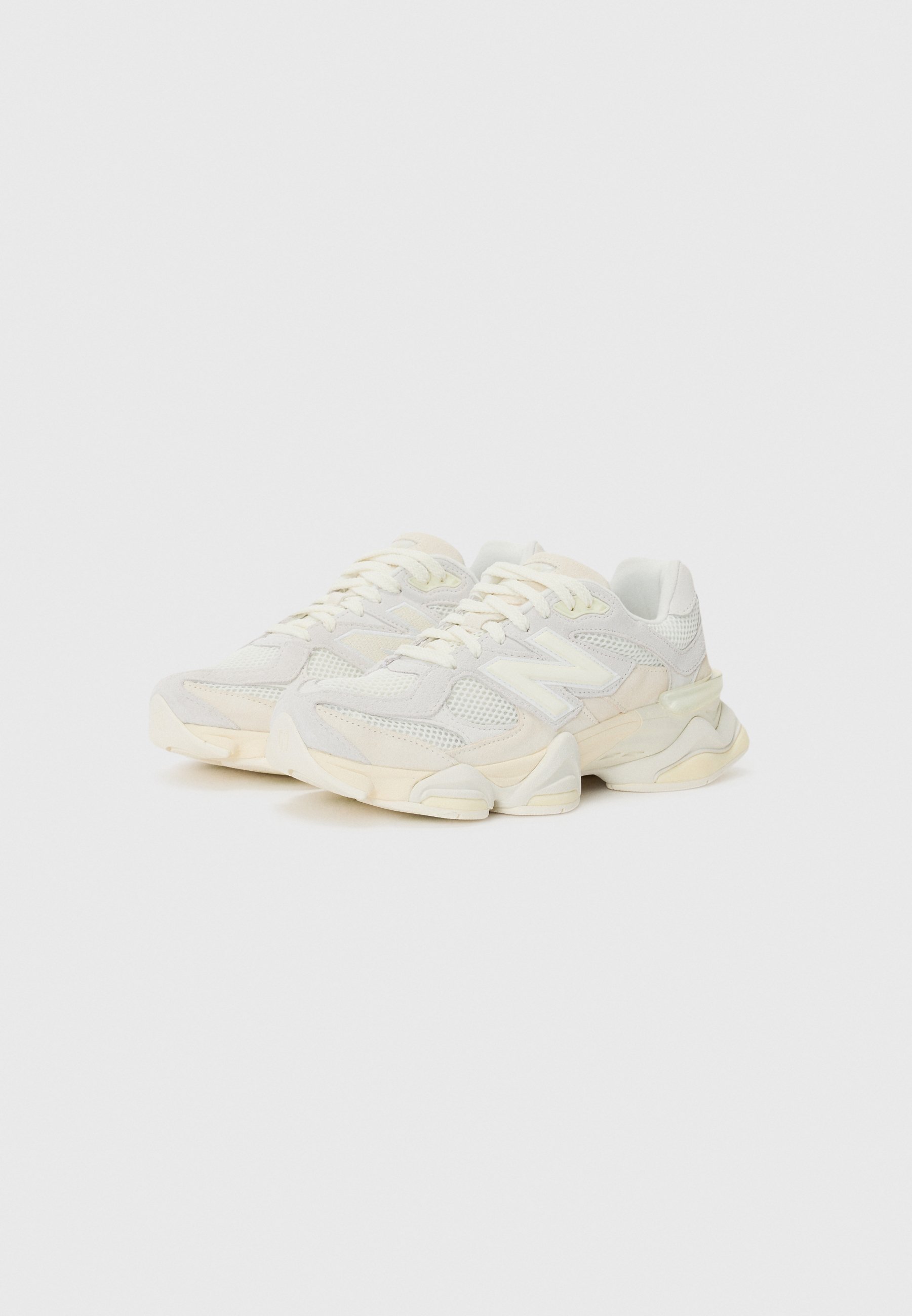 Zapatillas blancas voluminosas con una parte superior de malla, acentos de gamuza y suela de goma crema. Diseño de cordones con una destacada marca en el costado.