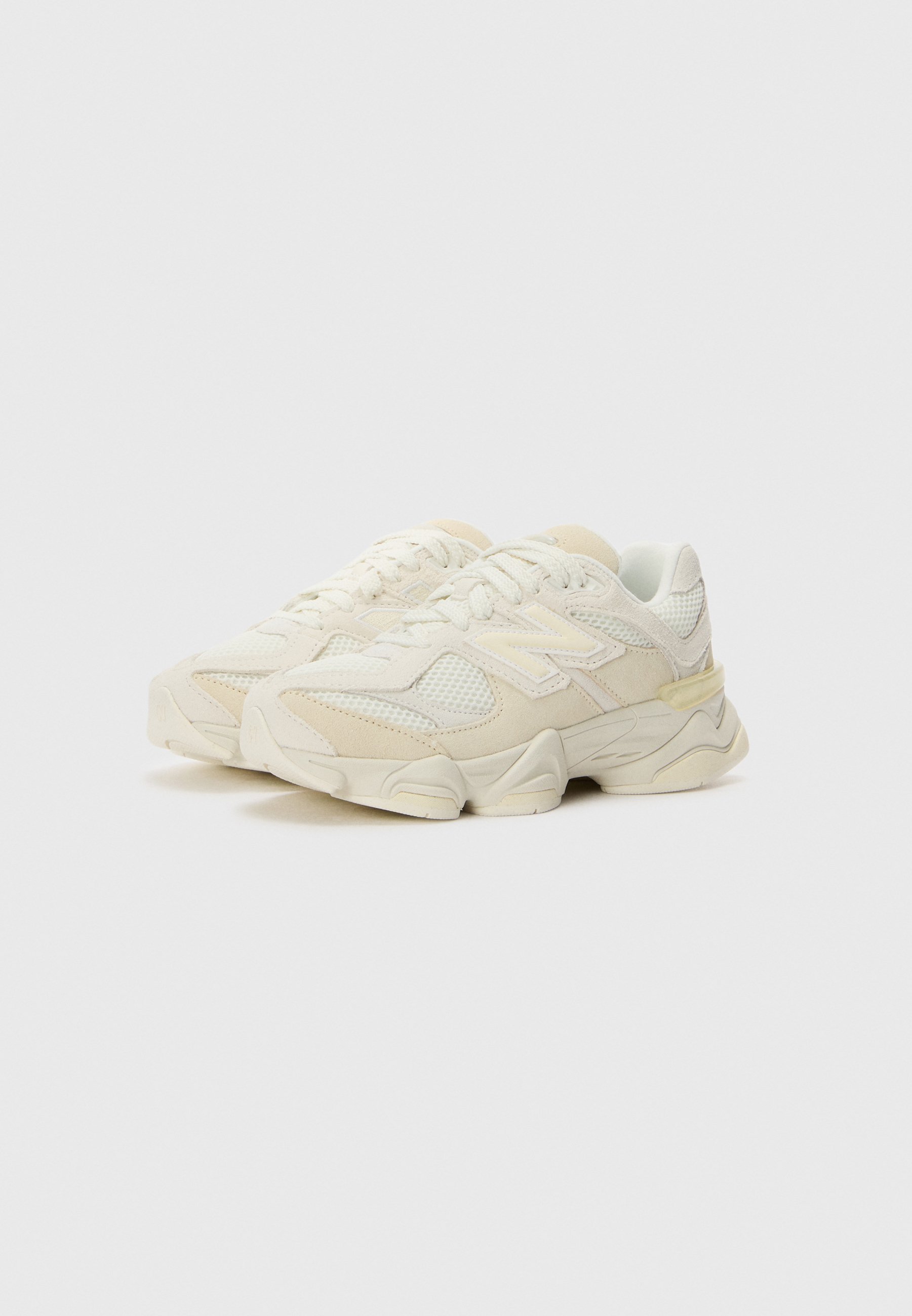 Par de zapatillas New Balance blanco hueso con suelas gruesas y detalles de malla, ligeramente inclinadas hacia la derecha sobre un fondo liso y claro.