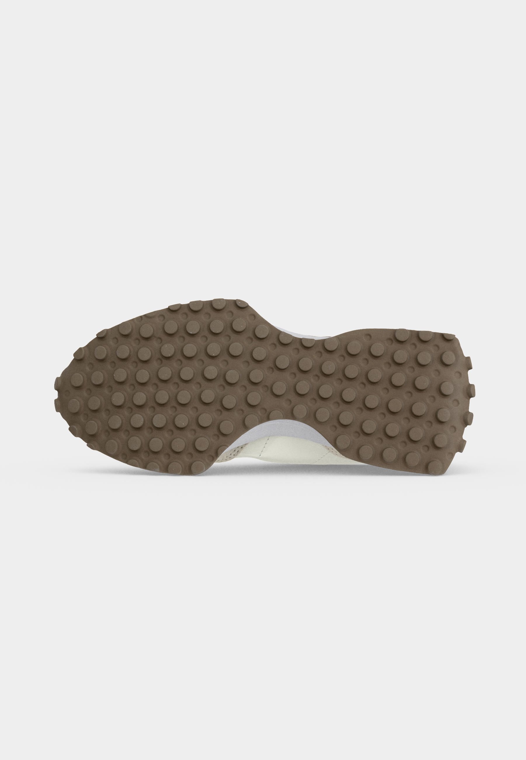 Suela de zapato con suela exterior de goma marrón con tacos redondos para agarre, vista desde abajo sobre un fondo blanco.