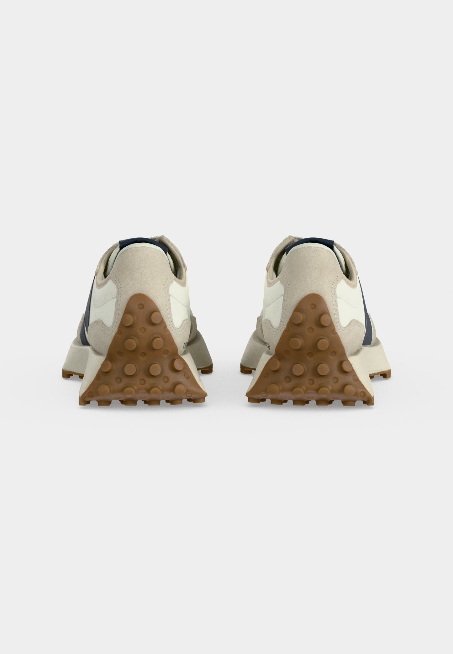 Par de zapatillas color blanco roto vistas desde el talón, con detalles de ante beige y suelas de goma marrón texturizadas con agarres circulares.