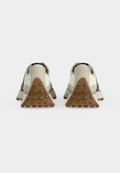 Par de zapatillas color blanco roto vistas desde el talón, con detalles de ante beige y suelas de goma marrón texturizadas con agarres circulares.