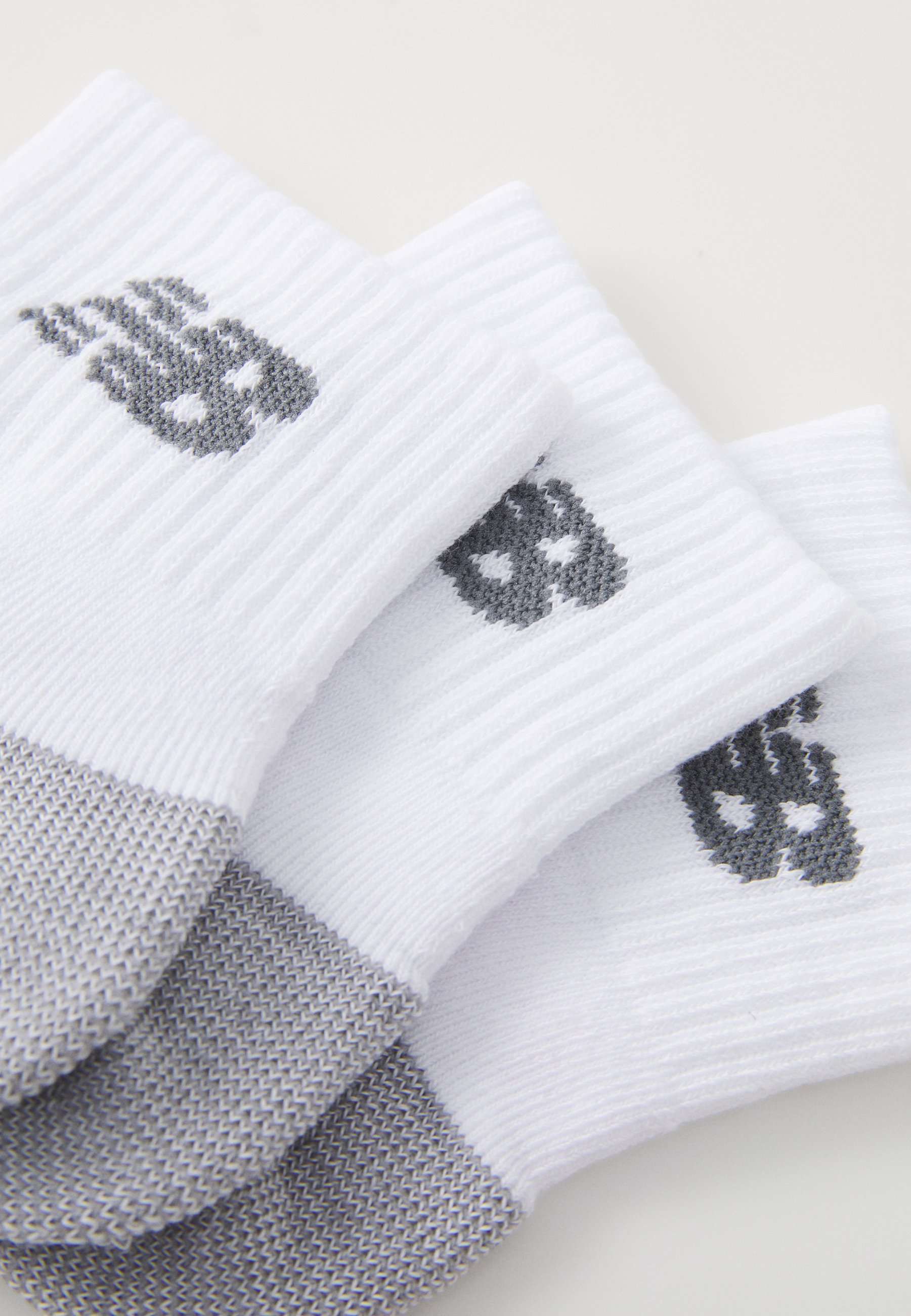 Tres pares de calcetines blancos y grises con diseños de calaveras en los puños, dispuestos de manera superpuesta sobre una superficie blanca.