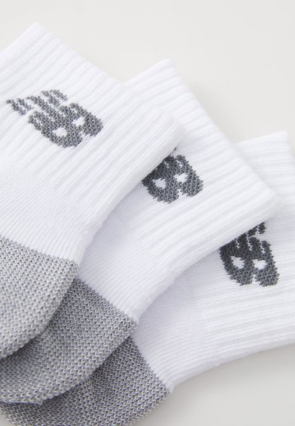 Tres pares de calcetines blancos y grises con diseños de calaveras en los puños, dispuestos de manera superpuesta sobre una superficie blanca.