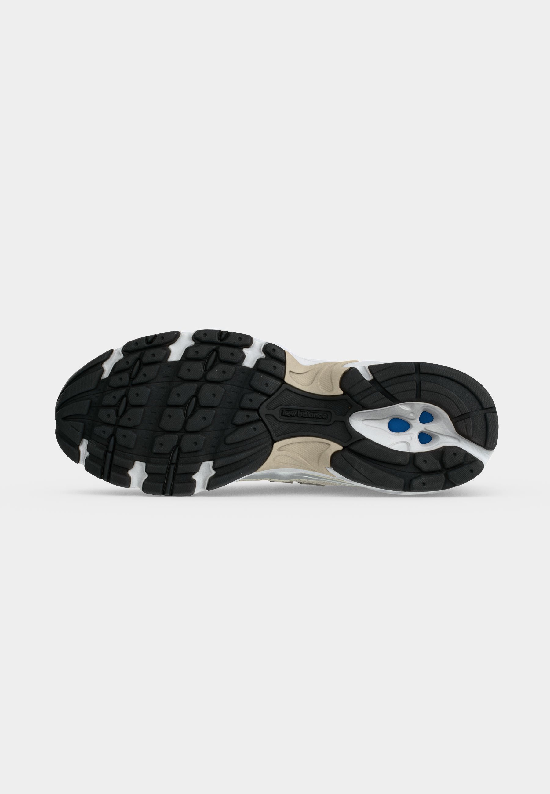 Suela de un zapato deportivo beige y negro con suela texturizada y detalles azules en el talón para agarre y soporte.