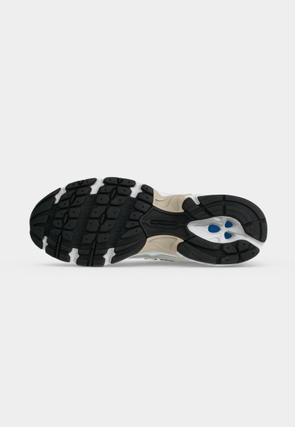 Suela de un zapato deportivo beige y negro con suela texturizada y detalles azules en el talón para agarre y soporte.