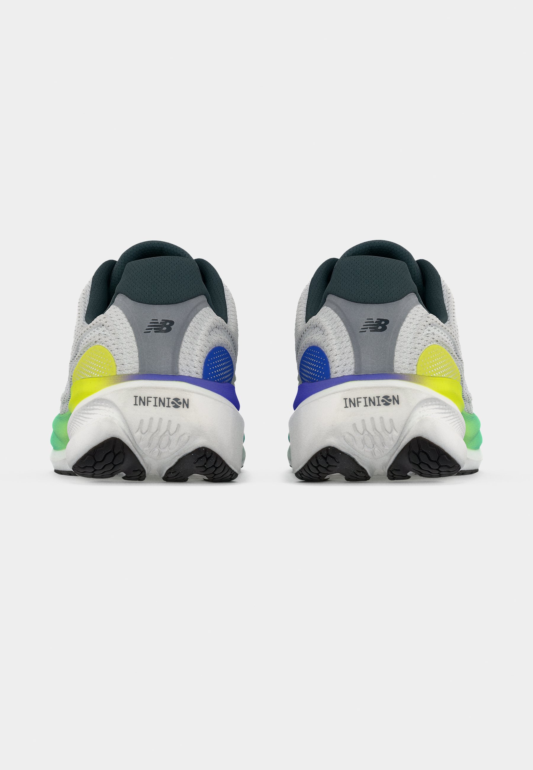 Par de zapatillas para correr New Balance grises y blancas con suelas negras, acentos azul y amarillo, vistas desde atrás sobre un fondo blanco.