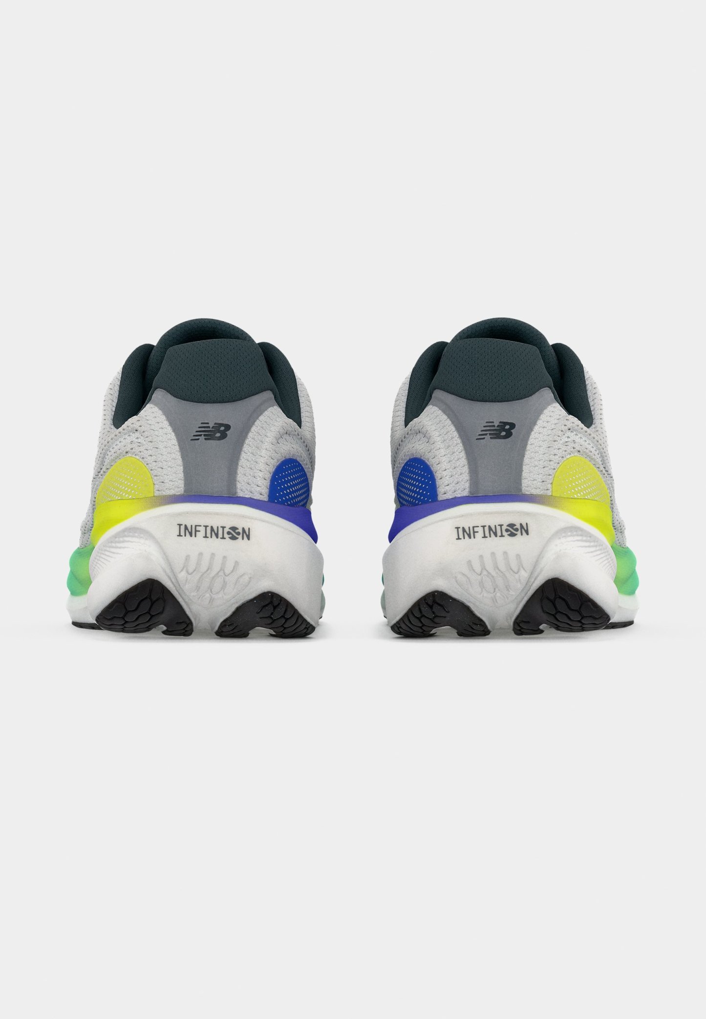 Par de zapatillas para correr New Balance grises y blancas con suelas negras, acentos azul y amarillo, vistas desde atrás sobre un fondo blanco.