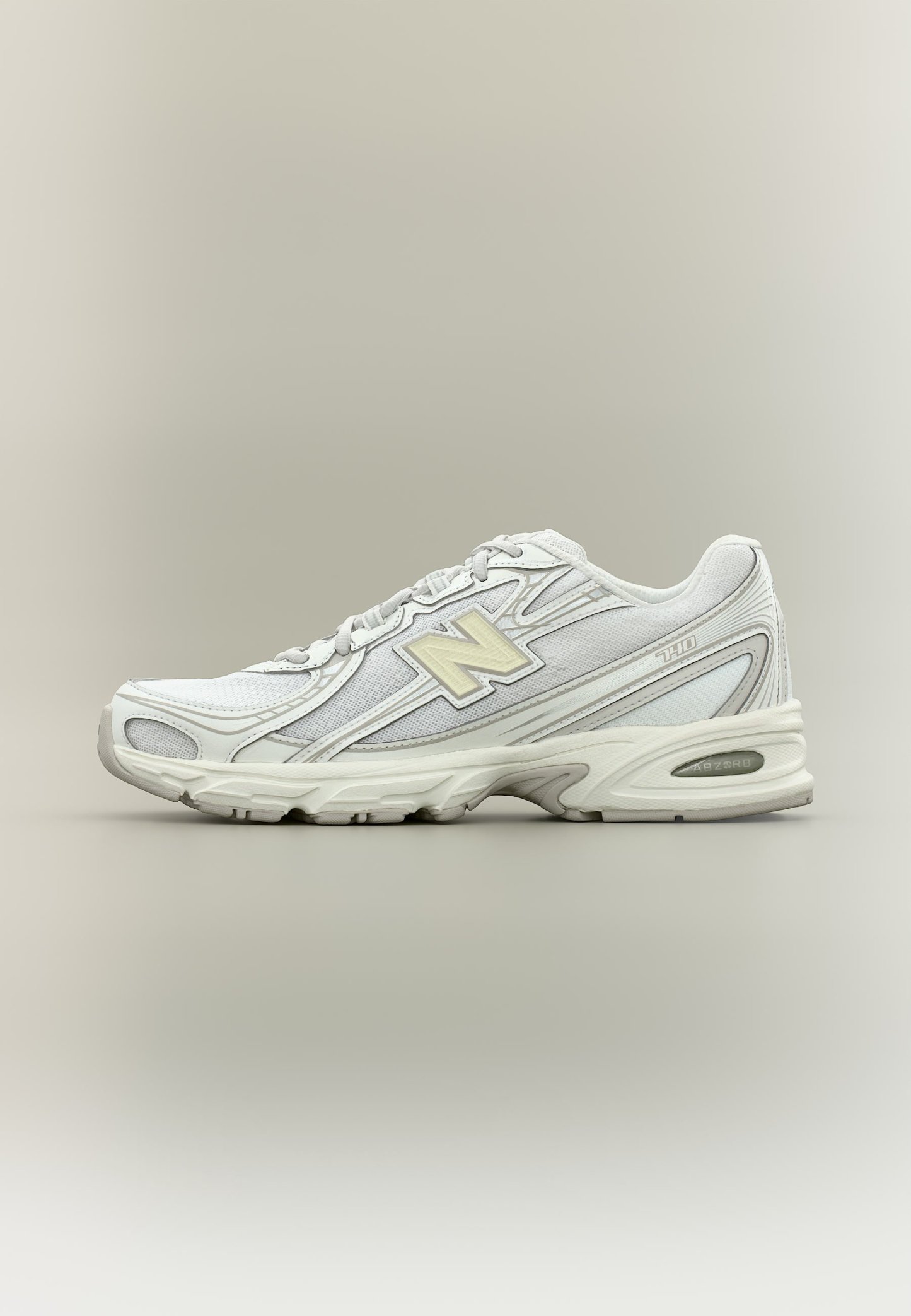 Zapatilla de running New Balance blanca y gris claro con paneles de malla, cordones y suela acolchada sobre un fondo neutro.