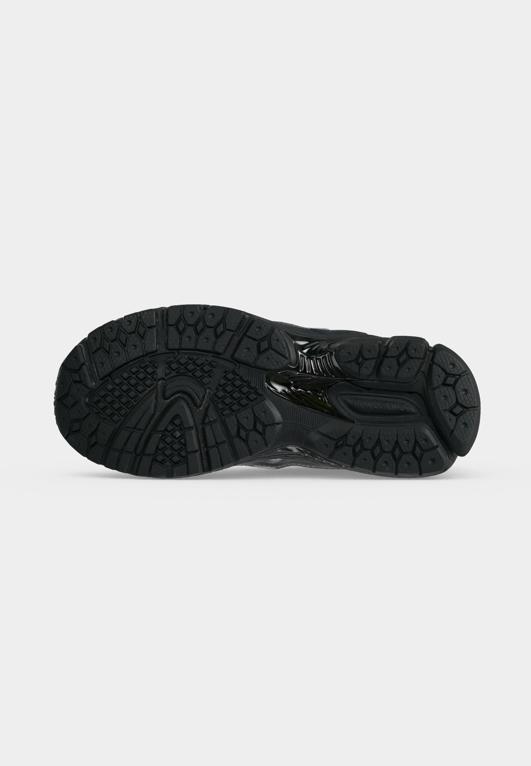 Suela negra de zapato deportivo con patrones texturizados para mejor agarre, mostrada desde abajo sobre un fondo blanco liso.