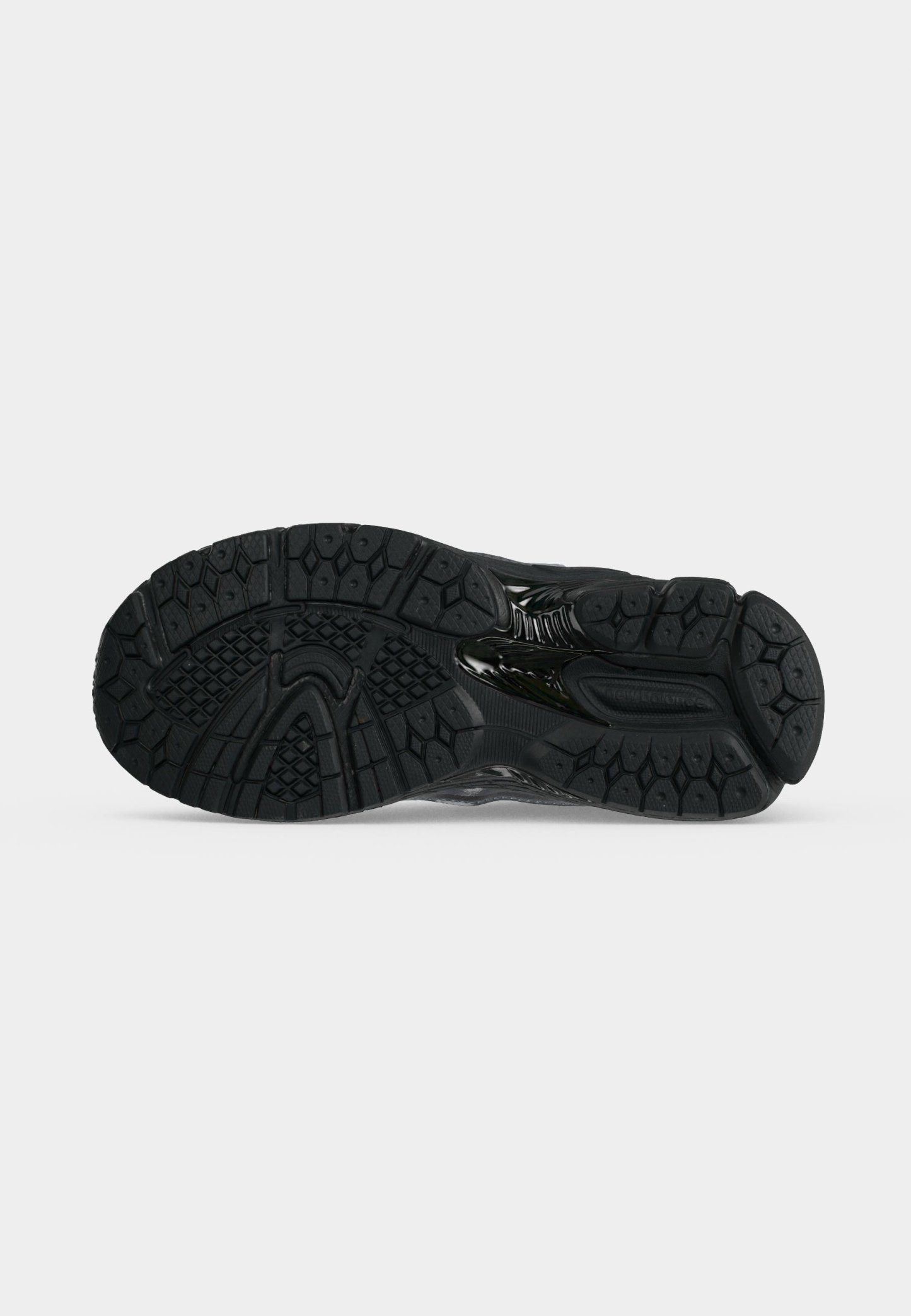 Suela negra de zapato deportivo con patrones texturizados para mejor agarre, mostrada desde abajo sobre un fondo blanco liso.