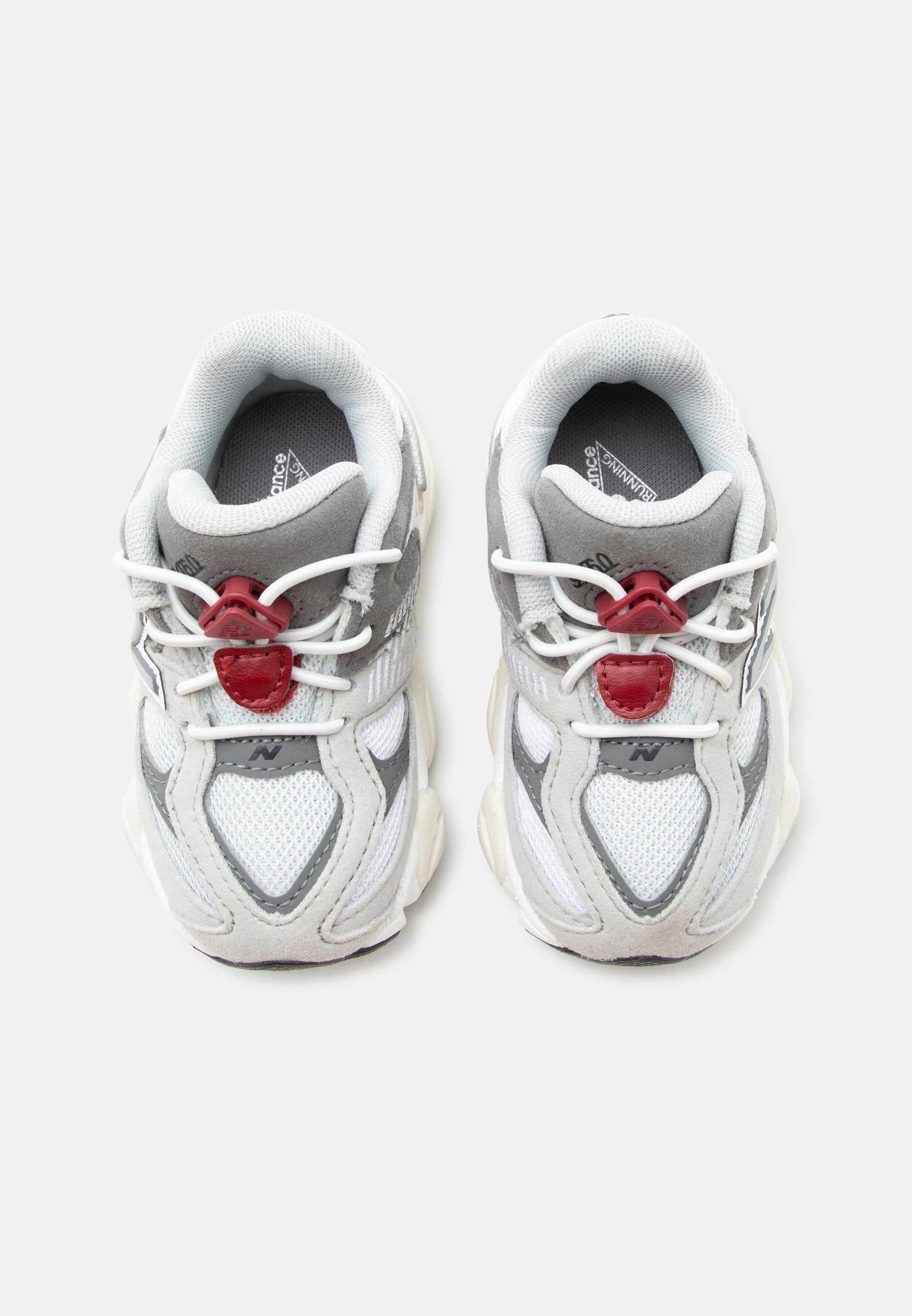 Par de zapatillas de running blancas y grises con cierres rojos para cordones, parte superior de malla y suelas acolchadas colocadas una al lado de la otra sobre un fondo blanco.
