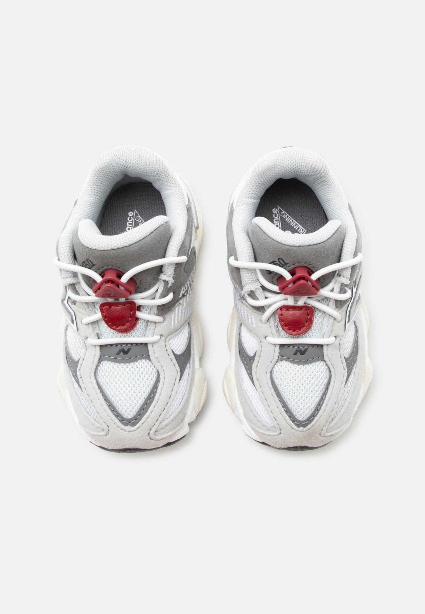 Par de zapatillas de running blancas y grises con cierres rojos para cordones, parte superior de malla y suelas acolchadas colocadas una al lado de la otra sobre un fondo blanco.