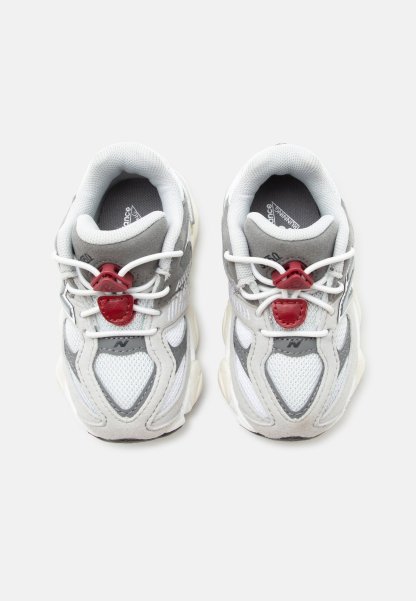 Par de zapatillas de running blancas y grises con cierres rojos para cordones, parte superior de malla y suelas acolchadas colocadas una al lado de la otra sobre un fondo blanco.