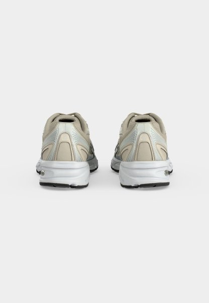 Par de zapatillas deportivas beige y blancas vistas por detrás sobre un fondo liso gris claro.