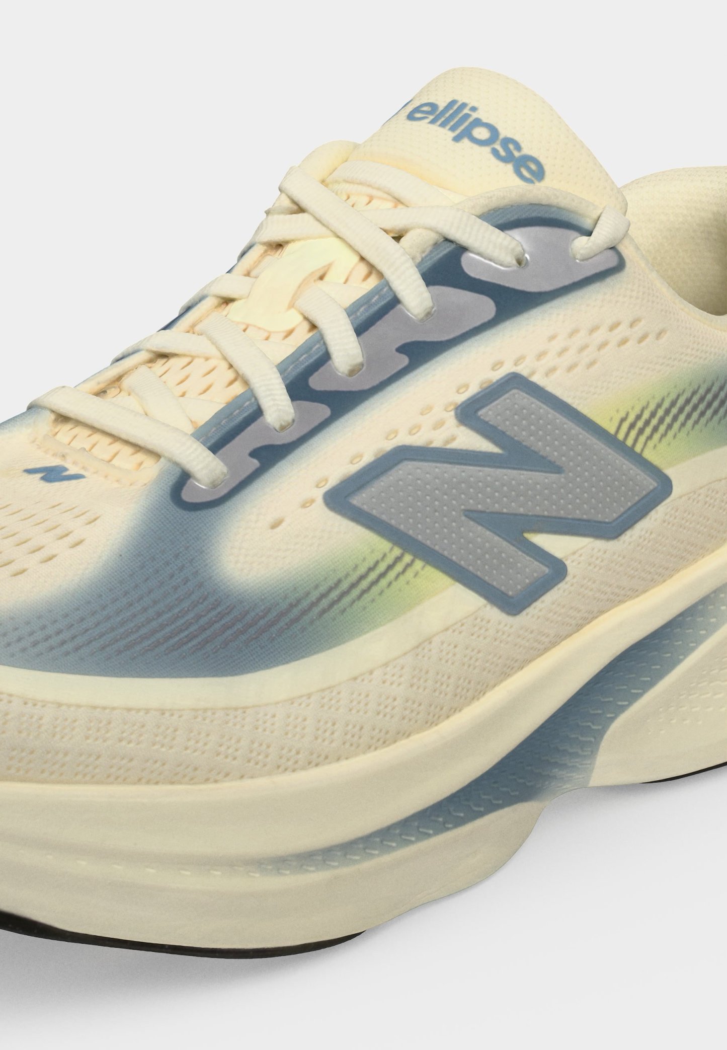 Zapatilla de running New Balance en beige claro y azul con cordones, suela texturizada y logo "N" en el lateral, nombre del modelo "ellipse" en la lengüeta.