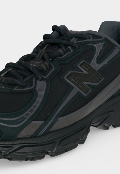 Zapatilla deportiva negra y gris con suela gruesa, cordones negros y logotipo texturizado "N" en el lateral.
