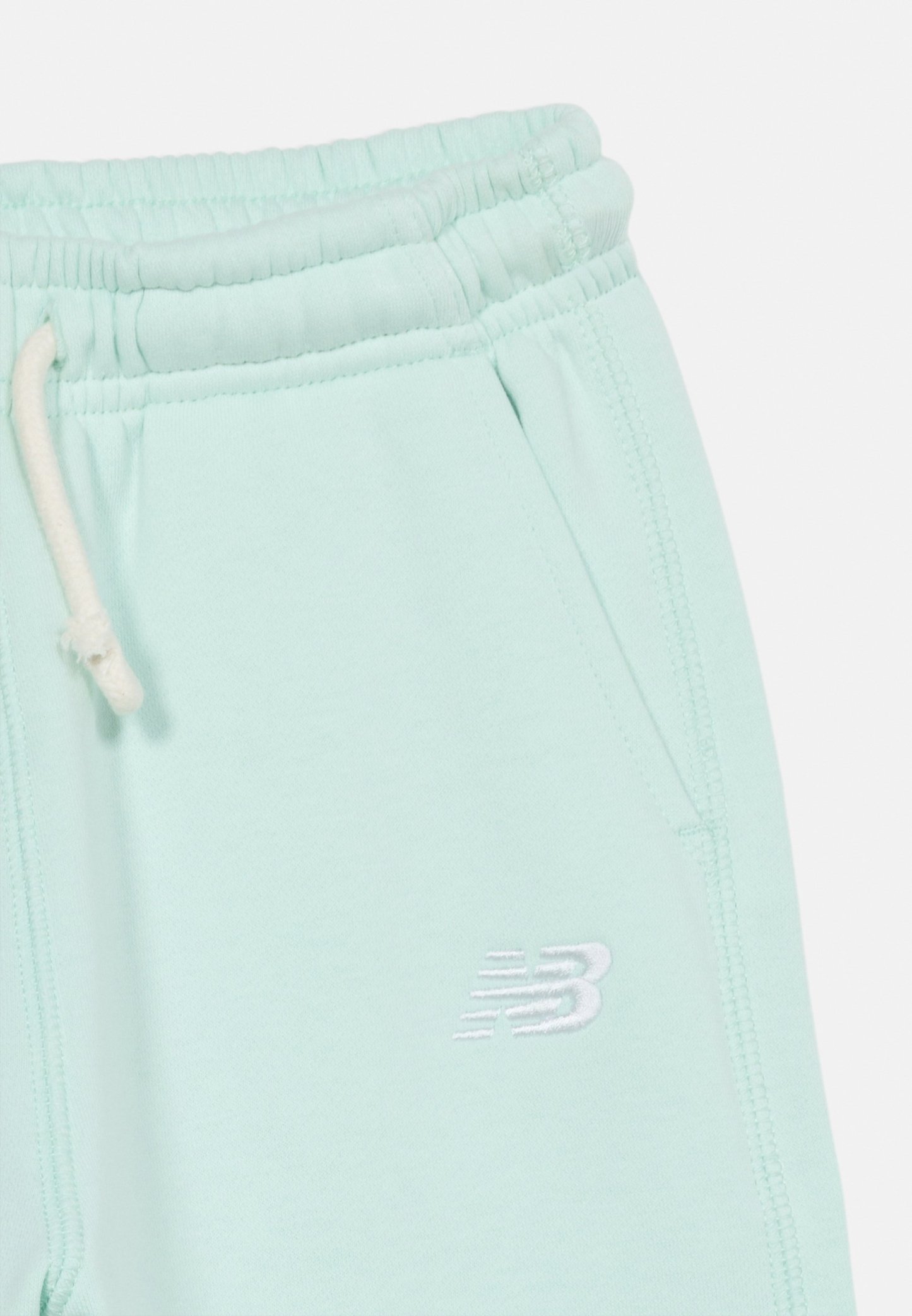 Pantalones deportivos con cintura elástica de color azul claro, cordón blanco y logo "NB" bordado en blanco cerca del bolsillo.