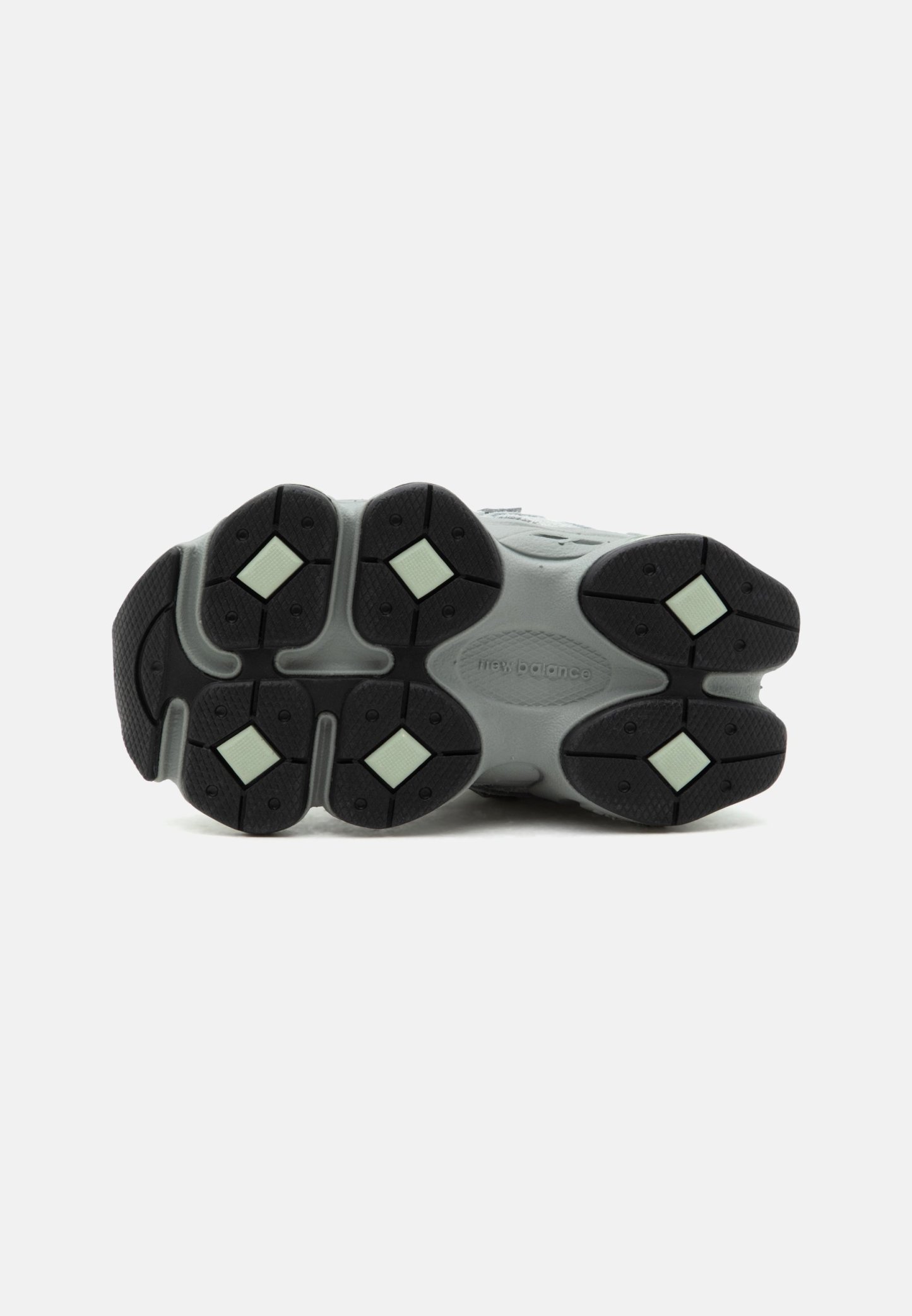 Suela de zapatilla New Balance gris y negra con patrones de dibujo en forma de diamante de color verde claro sobre un fondo blanco.