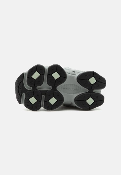 Suela de zapatilla New Balance gris y negra con patrones de dibujo en forma de diamante de color verde claro sobre un fondo blanco.