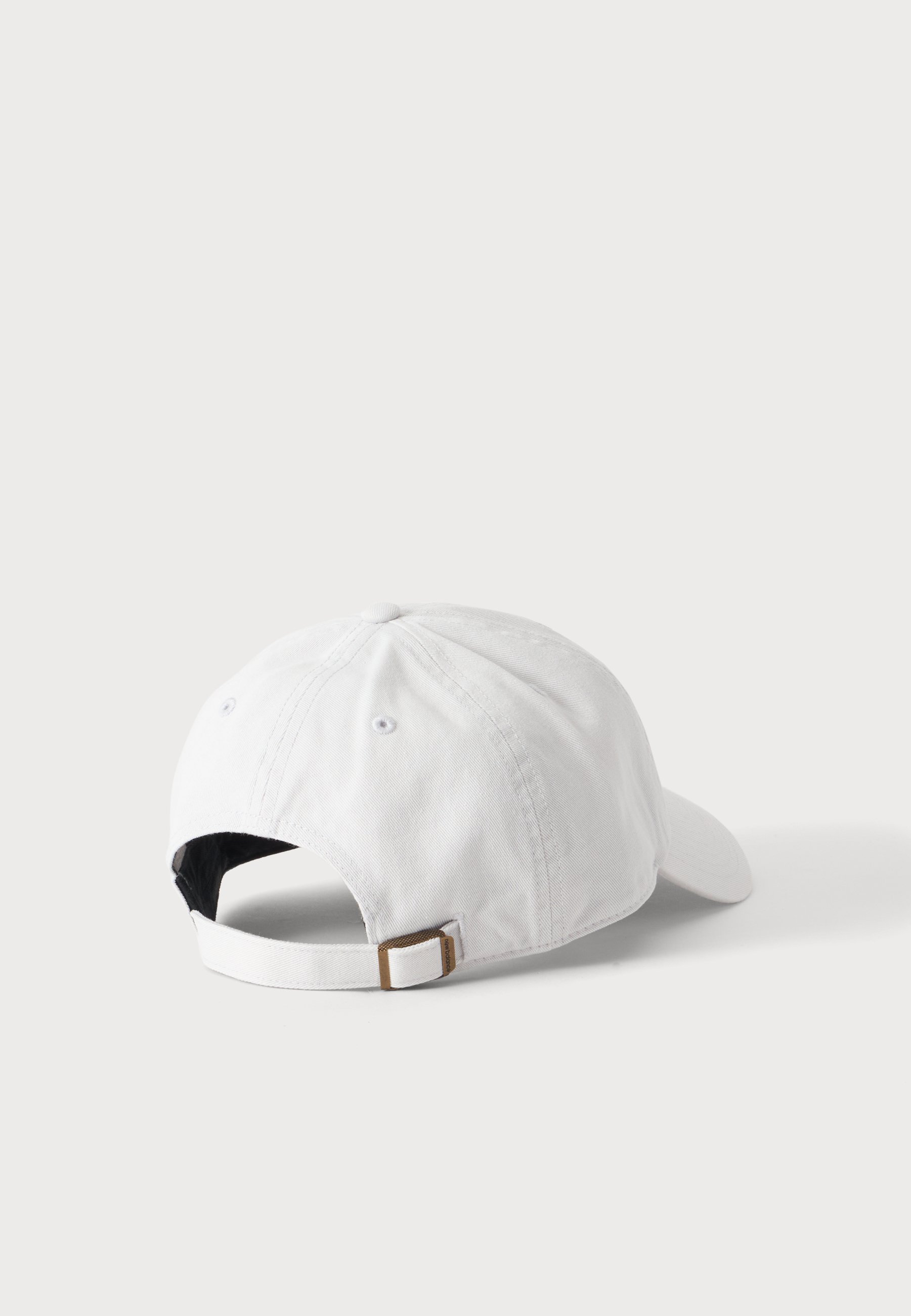 Gorra de béisbol blanca mostrada desde atrás con una correa de tela ajustable y hebilla de metal sobre un fondo claro y liso.