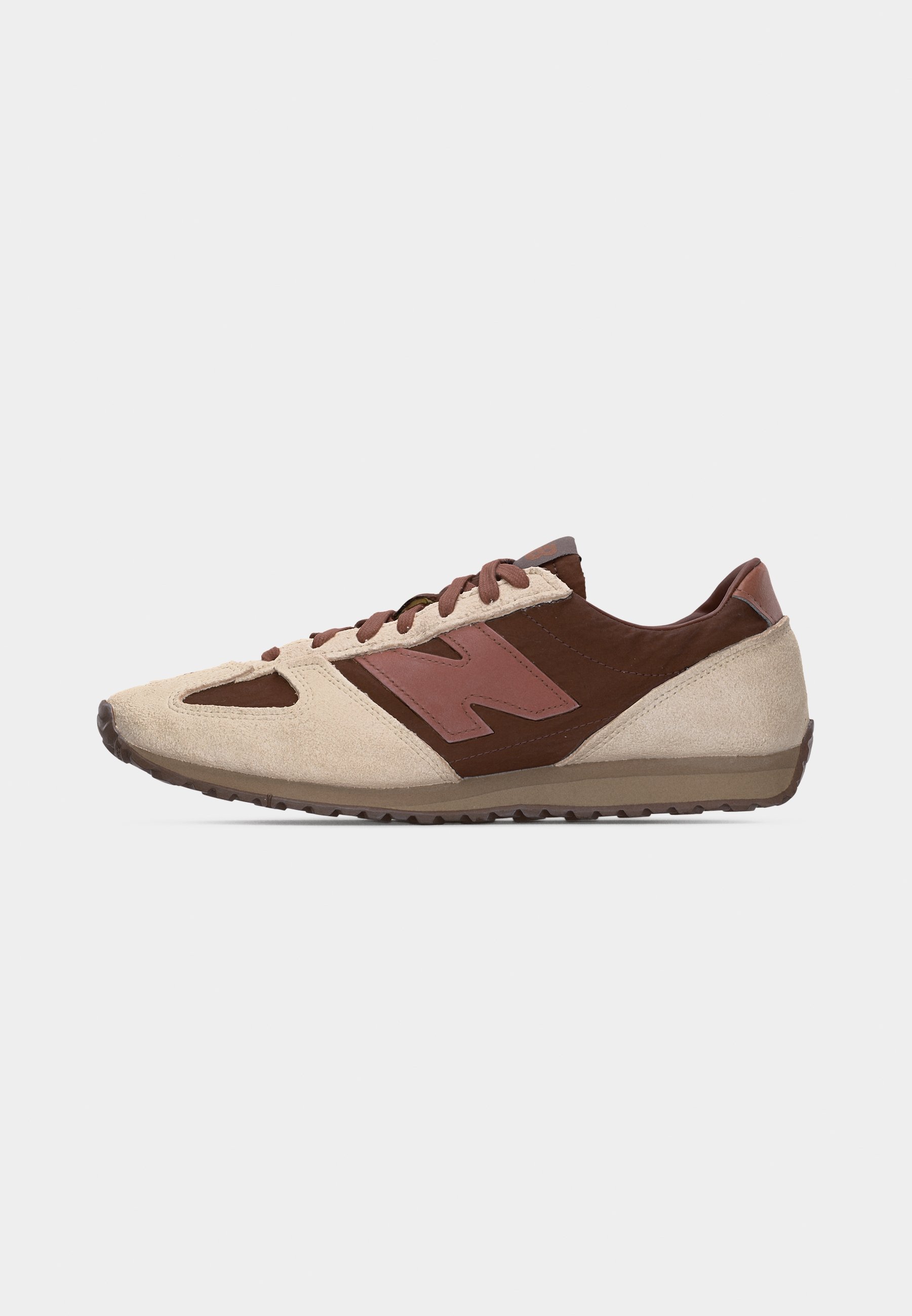 Zapatilla de ante beige y marrón con cordones en la parte delantera, suela de goma y un logotipo "N" marrón en el lateral, mostrada en vista de perfil izquierdo.