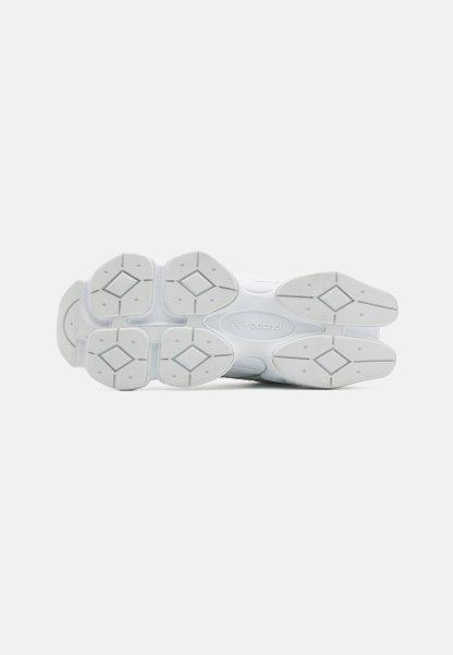 Suela de zapato deportivo blanco con patrón de goma texturizada, con formas de diamante y el logotipo de "New Balance" en la entresuela.