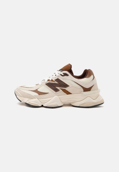 Zapatilla New Balance blanca y marrón con suela gruesa, cierre de cordones y detalles en malla y piel en la parte superior sobre un fondo liso.