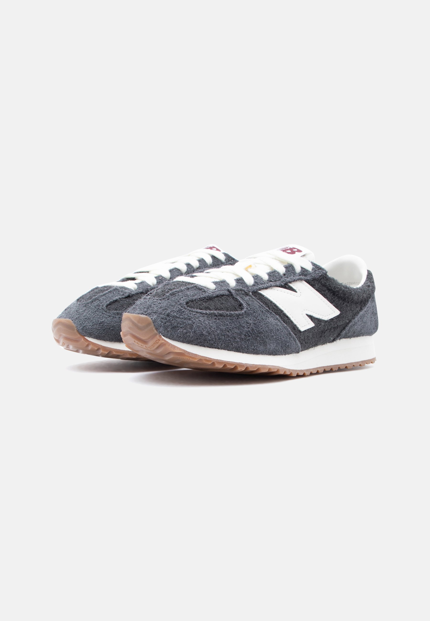 Par de zapatillas New Balance de color gris oscuro con cordones blancos, logo "N" blanco y suelas de color goma sobre un fondo blanco.